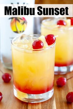 two glasses filled with drinks and cherries on top of a wooden table next to a bottle