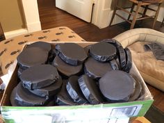 a box filled with lots of black round cushions on top of a wooden floor next to a dog bed