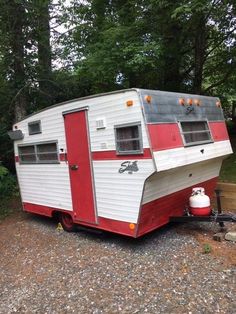 a red and white trailer parked on gravel next to trees