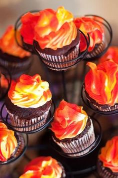 cupcakes with orange and yellow frosting are arranged on a cake stand in rows