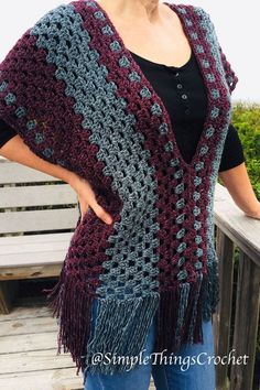 a woman wearing a crocheted shawl standing on a wooden bench with her hands in her pockets