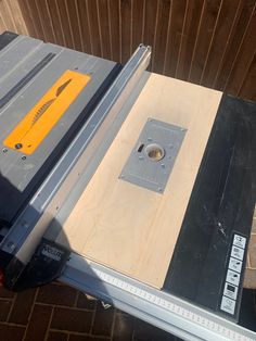 a table sawing machine sitting on top of a piece of wood next to a brick wall