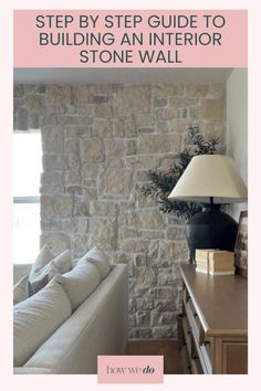 a white couch sitting next to a lamp on top of a wooden table in front of a stone wall