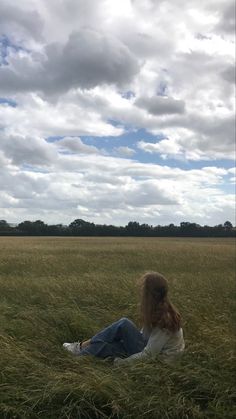 a woman sitting in the middle of a field with a kite flying over her head