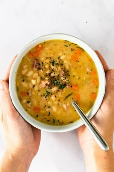 two hands holding a bowl of soup on a white table