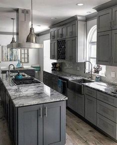 a large kitchen with gray cabinets and marble counter tops is pictured in this image, there are two pendant lights hanging over the island