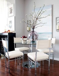 a dining room table with four chairs and a vase on top of the glass table