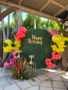 a happy birthday sign surrounded by balloons and greenery