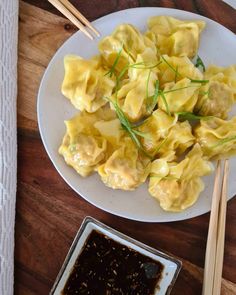 a white plate topped with dumplings and chopsticks next to a bowl of sauce