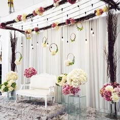 a white couch sitting under a wooden trellis next to flowers and greenery in vases