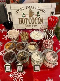 a red table topped with lots of different types of candies and chocolates next to a sign that says christmas blend hot cocoa