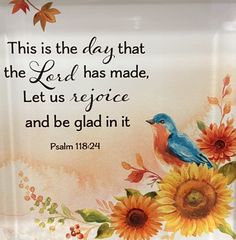 a painting with flowers and a bible verse on the bottom right hand corner is an image of a blue bird surrounded by sunflowers, which reads this is the day that the lord has made, let us