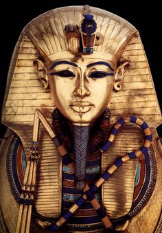 an egyptian mask with gold and blue designs on it's face is shown in front of a black background