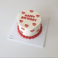 a white birthday cake with red hearts on it sitting on top of a card board