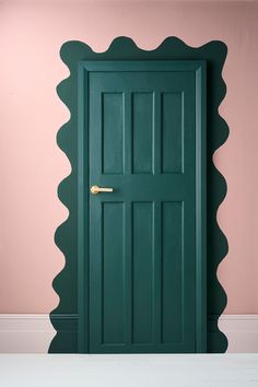 a green door with scalloped edges in a pink room