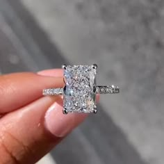 a person holding a ring with a cushion cut diamond in it's middle finger