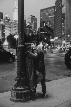 black and white photograph of two people kissing on the street corner in front of tall buildings