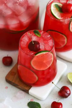 two glasses filled with red liquid and garnished with cherries, limes, and cherry slices