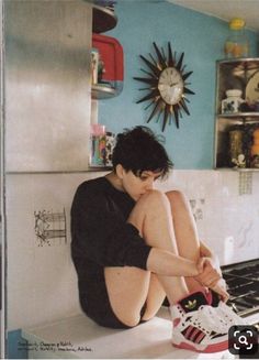 a young man sitting on the kitchen counter with his feet up in front of him