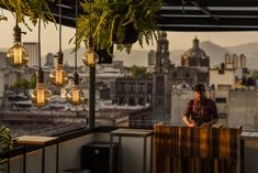 a man standing on top of a balcony next to plants and hanging lightbulbs