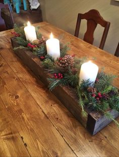 a wooden table topped with candles and greenery next to a candle holder filled with pine cones