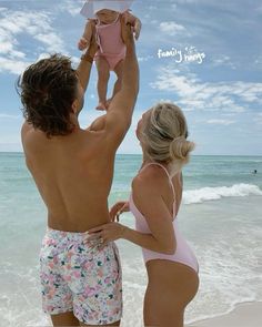 a man and woman holding a baby on the beach