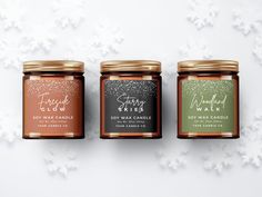 three jars of candles sitting next to each other on a table with snowflakes