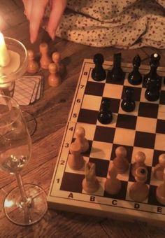 a chess board and wine glasses on a wooden table with someone playing the game in the background