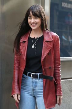 a woman wearing a red leather jacket and jeans is standing in front of a building