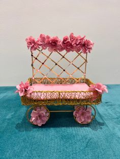 a miniature baby's carriage with pink flowers on the top and bottom, sitting on a blue carpet