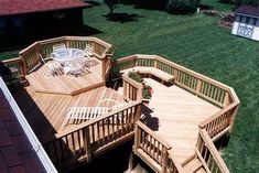 a large wooden deck with chairs and tables on it in the grass next to a house