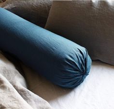 a blue pillow on top of a bed with white sheets and pillows in the background