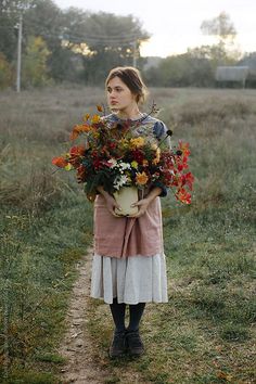 a woman standing in a field holding a bouquet of flowers