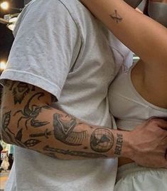 a man and woman hugging each other with tattoos on their arms in front of a mirror