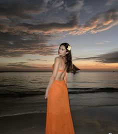 a woman standing on top of a beach next to the ocean in an orange dress