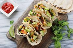 several tacos on a cutting board with salsa and avocado