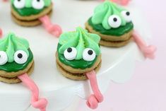 cookies decorated with green icing and googly eyes on a white cake platter