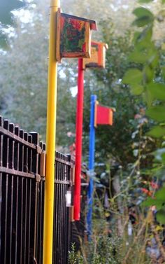 there is a yellow and red pole next to a black fence in the yard with trees behind it