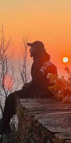 a man sitting on top of a wooden bench next to the ocean at sunset or sunrise