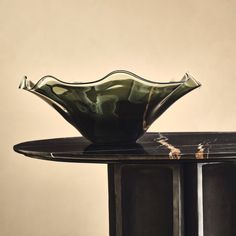 a green glass bowl sitting on top of a black table next to a white wall