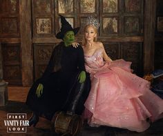 a woman in a pink dress sitting next to a man in a witch costume