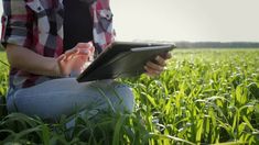 a woman sitting in the middle of a field using a tablet