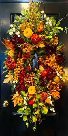 a wreath is hanging on the door with autumn flowers and leaves around it in front of a black door