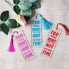 three bookmarks with tassels and flowers on a wooden table next to it