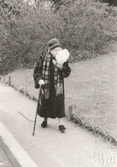 an old woman is walking down the street with her cane in hand and wearing a hat