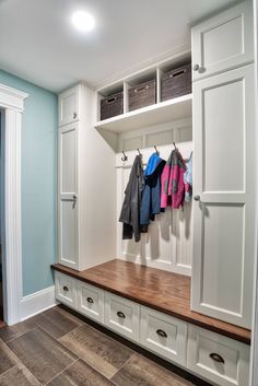 a mud room with white cabinets and coats hanging on the hooks in front of it