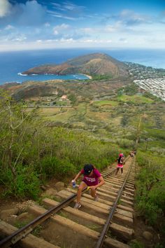 two people are climbing up some stairs near the water and hills in the distance, while another person is running down them