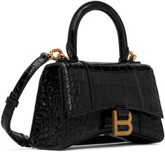 Find BALENCIAGA Hourglass Bag on Editorialist. The Balenciaga Hourglass Bag is crafted from croc-embossed calfskin. It features a rolled carry handle, adjustable and detachable shoulder strap, patch pocket at the back, curved base, logo hardware at the foldover flap, nappa lambskin lining, logo-engraved antiqued gold-tone hardware. The bag measures 5 inches in height, 7.25 inches in width, and 2.5 inches in depth. Balenciaga Hourglass Bag, Baggage Claim, Balenciaga Black, Black Xs, Handle Bag, Travel Luggage, Luggage Bags, Antique Gold, Patch Pocket