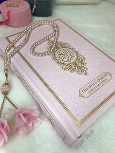 a pink book with pearls on it and a necklace hanging from the front, sitting on a white furnishing