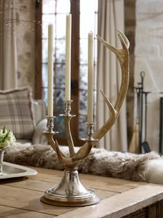 an antler candle holder on a wooden table in front of a fireplace with candles